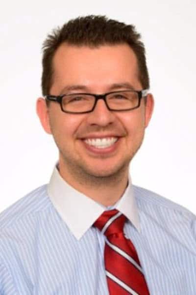 A smiling man wearing glasses and a red tie.